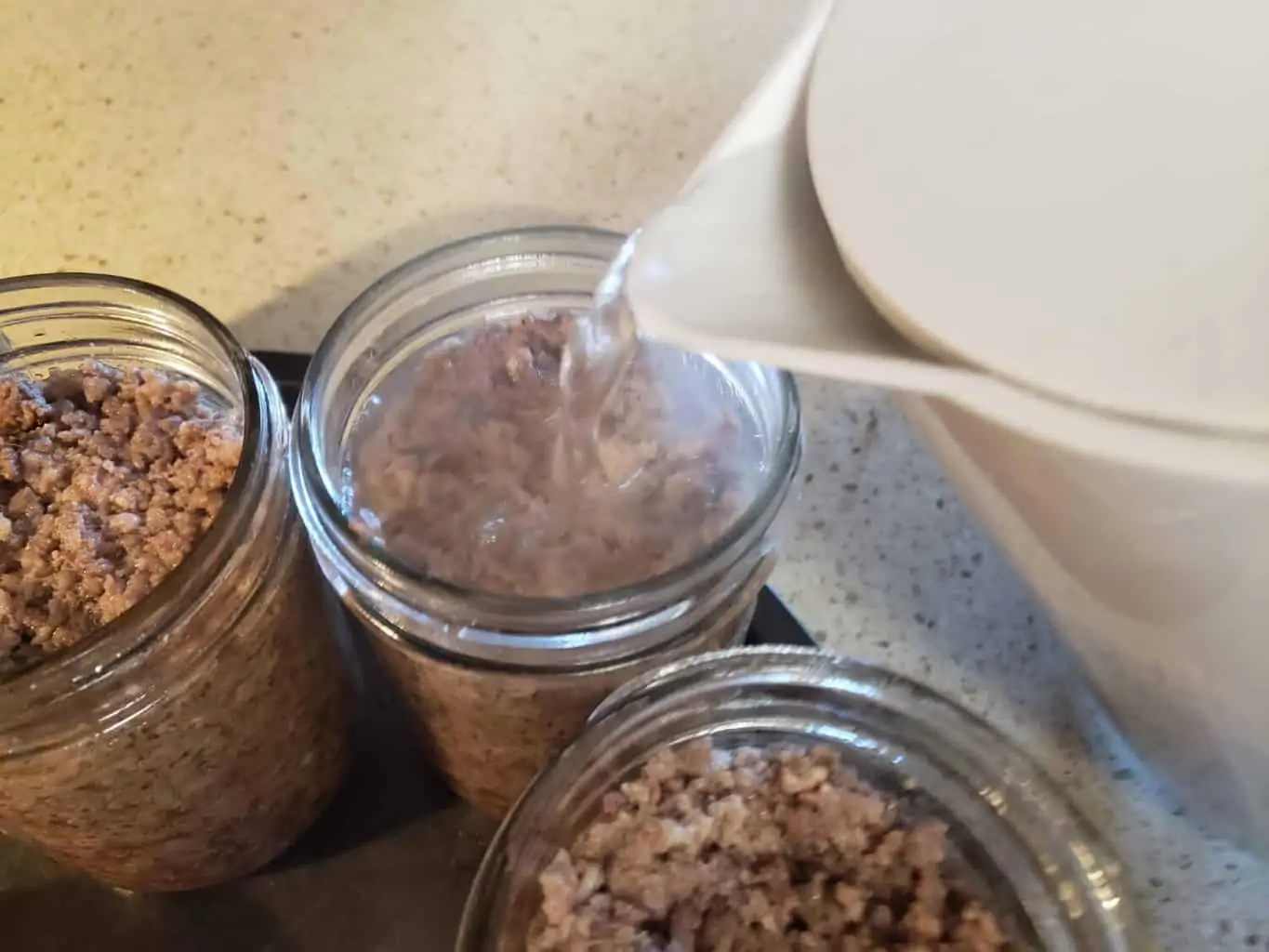 Adding boiling water to jars of ground meat for canning