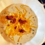 loaded potato soup in white bowl on wooden table with blue towel