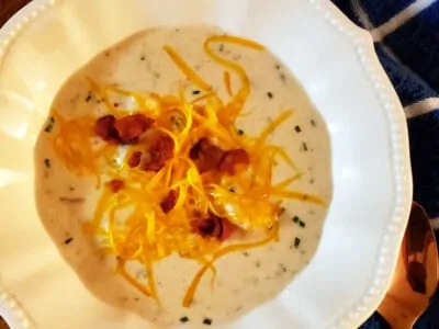 loaded potato soup in white bowl on wooden table with blue towel