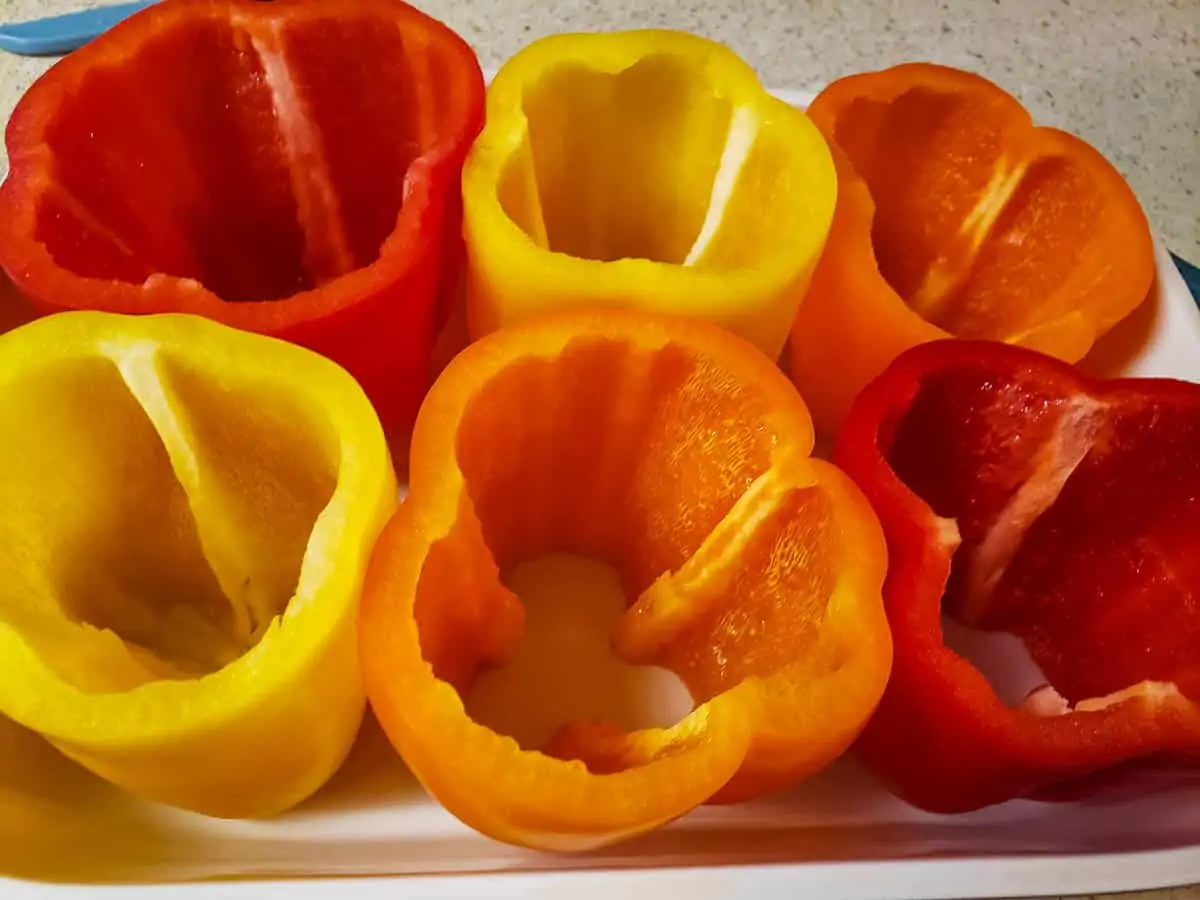 red, orange, and yellow bell peppers with tops cut off and seeds removed in baking dish